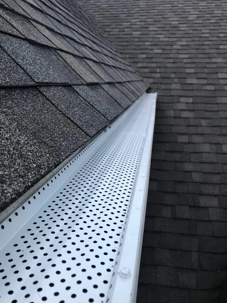 Perforated gutter protection beside an asphalt-shingle roof edge