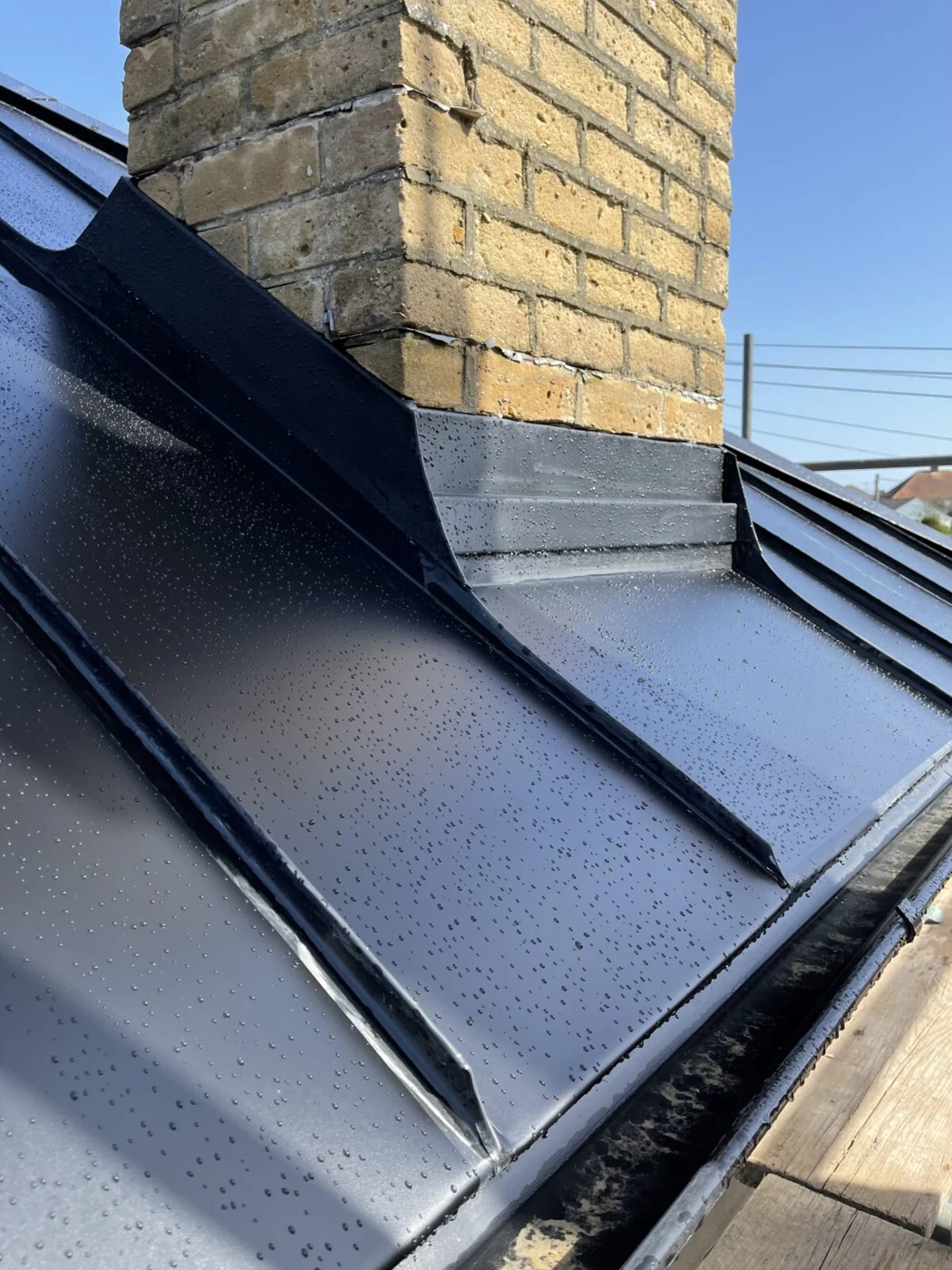Dark flashing around a brick chimney on a black Standing Seam metal roof