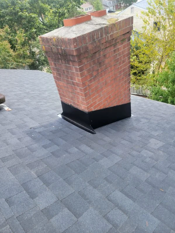 Dark chimney flashing against brick on an asphalt-shingle roof